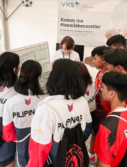 Eine Gruppe junger Fußballspieler aus den Philippinen sammelt sich um einen Informationsstand des VKS, um sich beim Bundesfinale der Soccer Liga auf Rügen über die Stammzellspende zu informieren